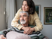 Daughter hugging senior father from behind holding hands