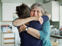 Elderly mom hugging her caregiver daughter in the kitchen